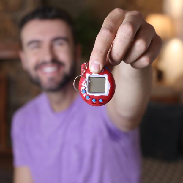 Ein Mann hält ein rotes Tamagotchi in die Kamera.