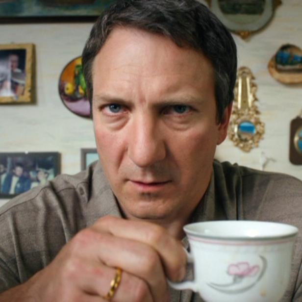 Ein Mann hält eine Teetasse in der Hand und blickt ernst in die Kamera.