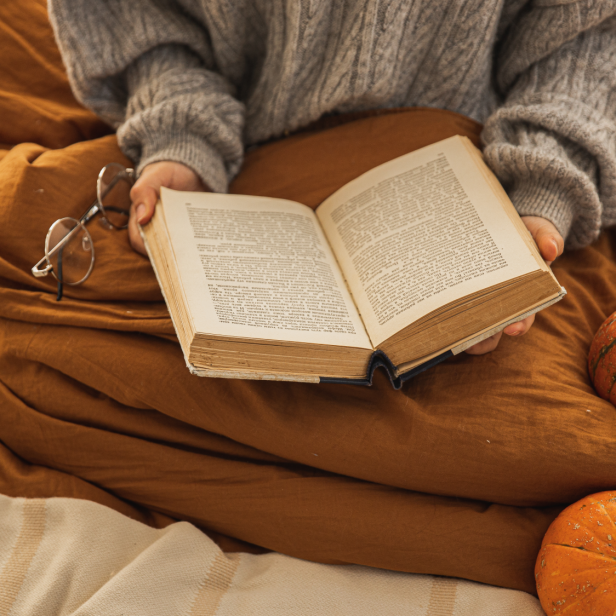 Eine Person liest ein Buch im Bett, neben ihr liegen zwei Kürbisse.