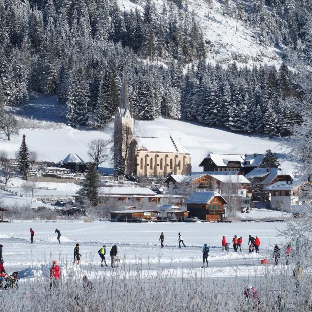 verschneite Landschaft am Weissensee in Kärnten, Eisläufer auf dem zugefrorenen See, Kirche im Hintergrund