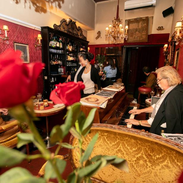 In einer Bar spielt ein Pianist, während eine Barkeeperin Getränke zubereitet.