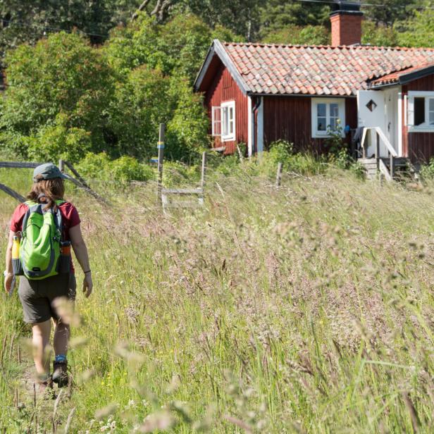 Frau beim Wandern auf den schwedischen Schären vor typisch schwedischem roten Haus