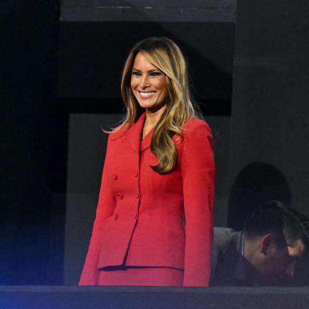 Melania Trump in einem roten Hosenanzug lächelt.