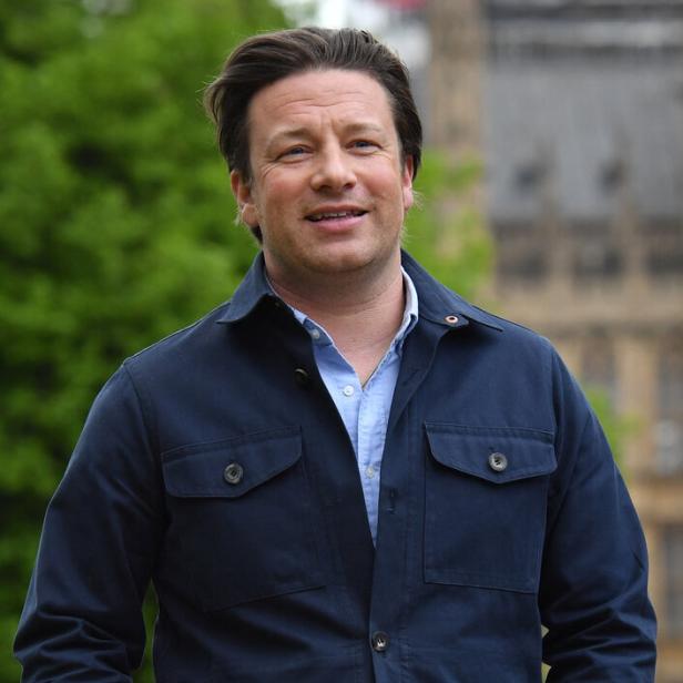 Jamie Oliver trägt eine blaue Jacke und Jeans.