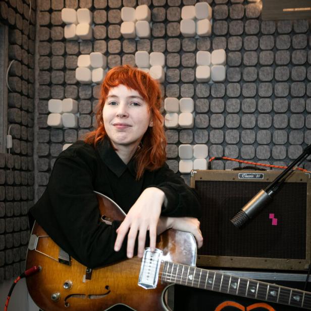 Mira Lu Kovacs mit Gitarre in einem Aufnahmestudio.