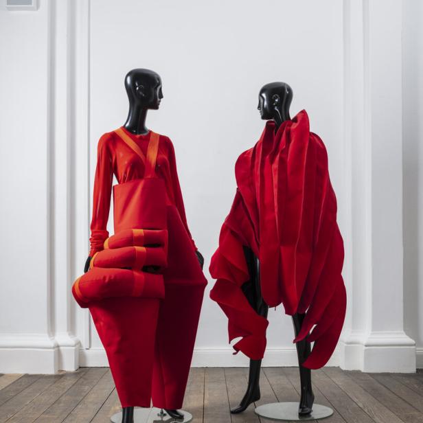 Zwei Schaufensterpuppen präsentieren extravagante, rote Mode vor einer weißen Wand.