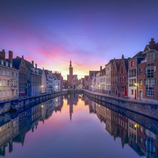 Ein Kanal in Brügge spiegelt die Gebäude und den Himmel bei Sonnenaufgang wider.