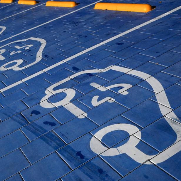 Blaue Parkplätze mit weißen Symbolen für Elektroautos und gelben Radstoppern.