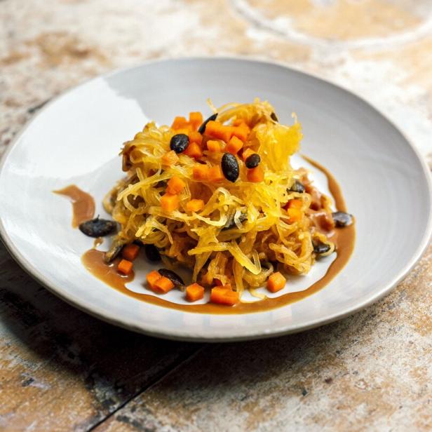 Spaghetti-Kürbis mit Karotten und schwarzen Oliven auf einem Teller.