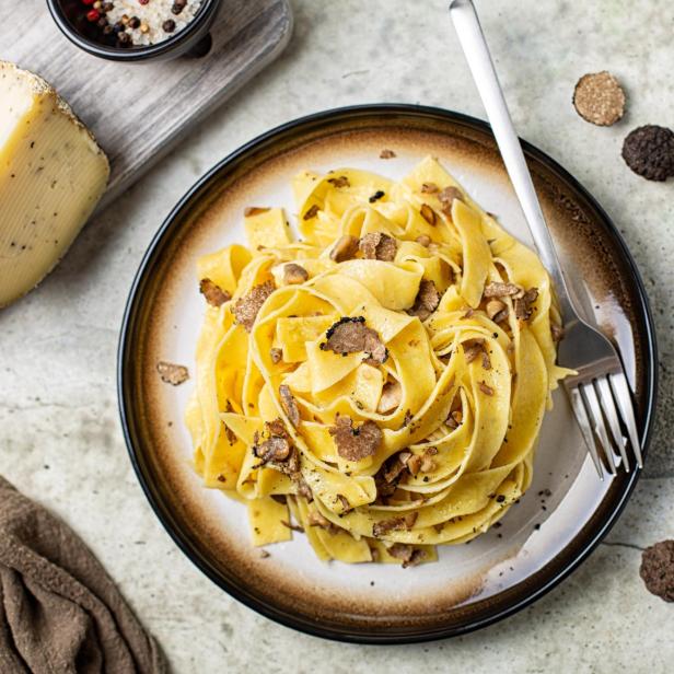 Ein Teller mit Trüffelpasta und ein Stück Trüffelkäse.