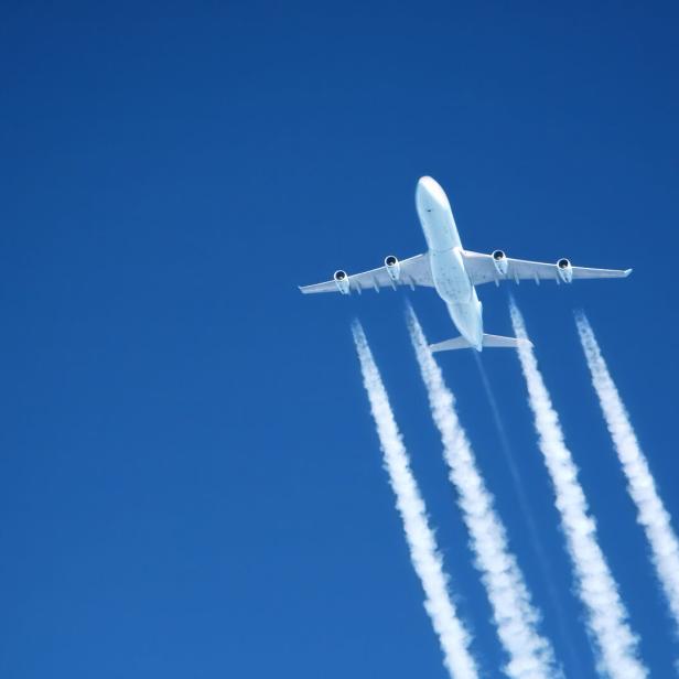 Ein Flugzeug zieht Kondensstreifen vor einem blauen Himmel hinter sich her.