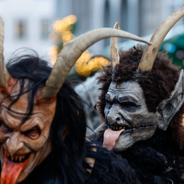 Zwei Krampusse mit furchteinflößenden Masken und Hörnern zeigen ihre Zungen.