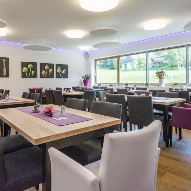 Ein Speisesaal mit gedeckten Holztischen und Stühlen in Grau und Lila.
