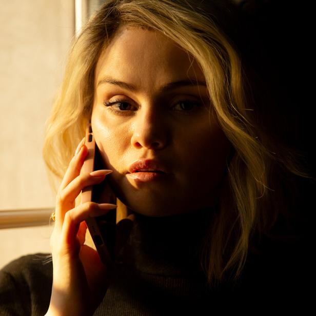 Eine blonde Frau telefoniert am Fenster.