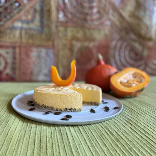 Eine Kürbis-Frischkäse-Torte auf einem Teller mit Kürbiskernen dekoriert.