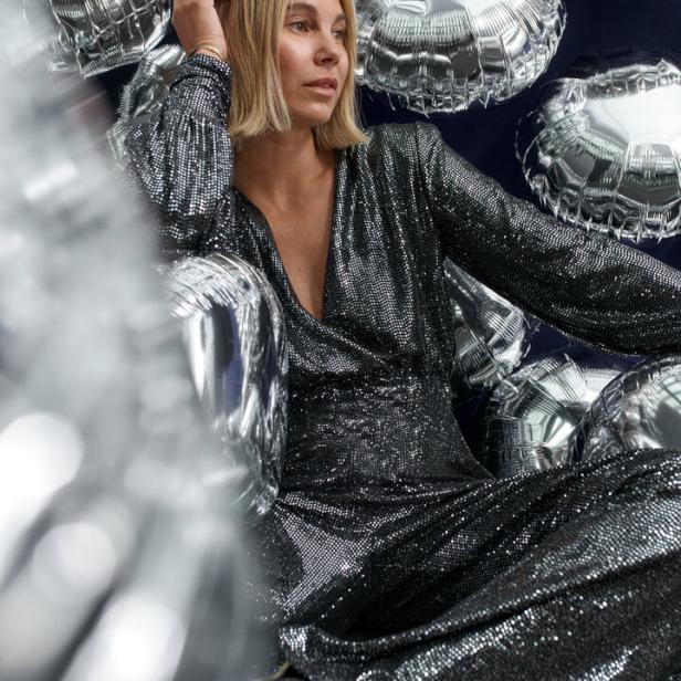 Eine Frau in einem glitzernden Kleid posiert vor silbernen Luftballons.