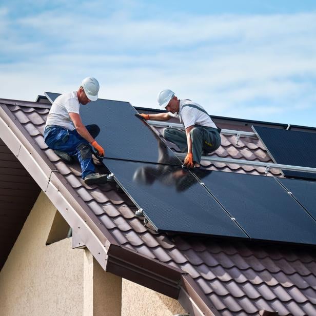 Arbeiter installieren Module für eine Photovoltaik-Anlage auf dem Dach eines Einfamilienhauses.