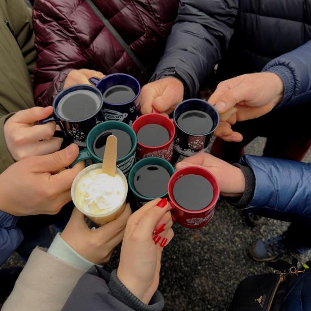 Mehrere Personen stoßen mit Tassen mit Glühwein und einem Getränk mit Sahne an.