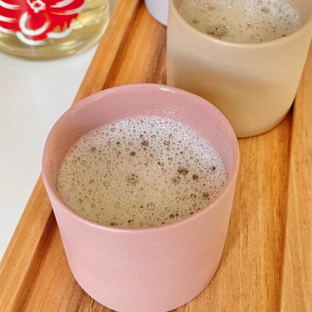 Mehrere Tassen mit schaumigen Getränken auf einem Holztablett, möglicherweise Tamagozake.