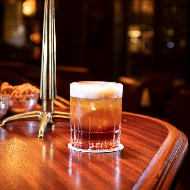 Ein Cocktail mit Schaum steht auf einem Holztisch neben einem Kerzenständer.