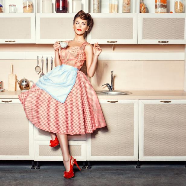 Eine Frau im Retro-Stil mit rotem Kleid und Schürze in einer Küche.