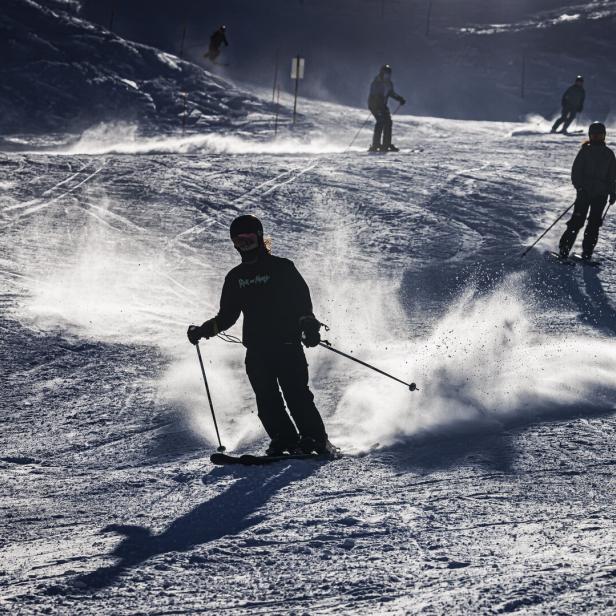 Skifahrer auf einer Skipiste mit aufgewirbeltem Schnee.