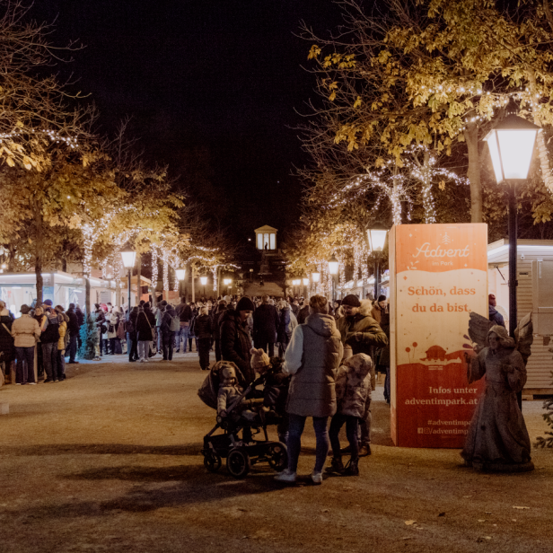 Eine beleuchtete Allee mit Weihnachtsmarktständen und Besucher:innen.