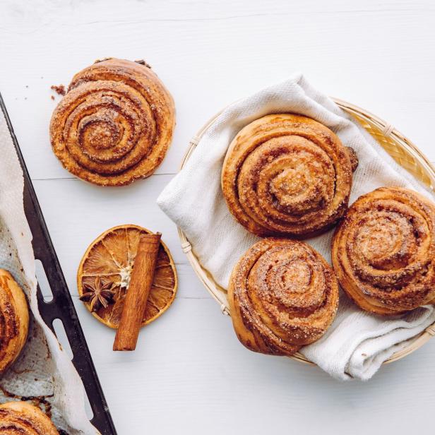 Zimtschnecken auf einem Backblech und in einem Korb mit Zimtstange und Orangenscheibe.