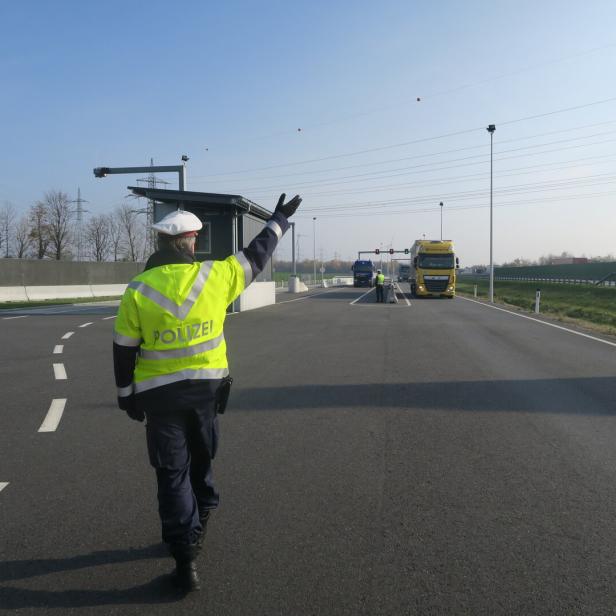 Ein Polizist in gelber Jacke winkt Lastwagen auf einer Autobahn durch eine Kontrollstelle.