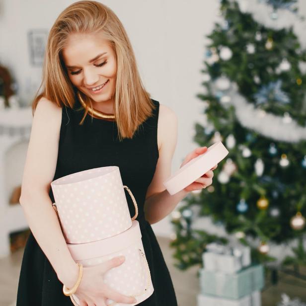 Eine hübsche Frau steht vor einem Weihnachtsbaum und freut sich über ein Geschenk.