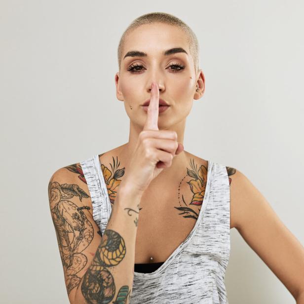 Eine junge Frau mit Tattoos hält den Finger vor den Mund.