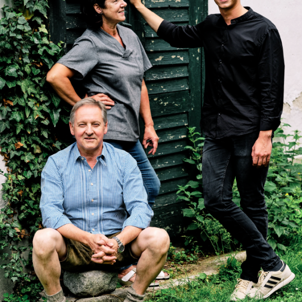 Drei Personen stehen im Gras vor einem Haus