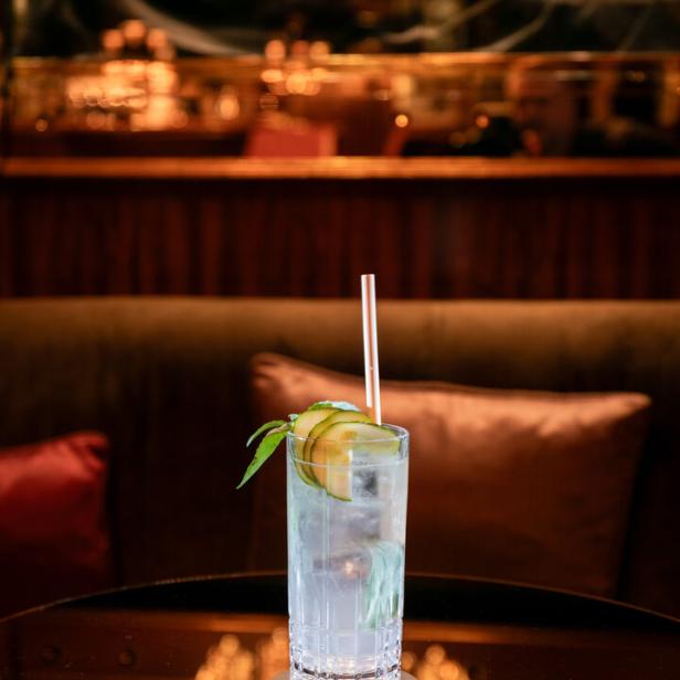 Ein Cocktail mit Gurke und Basilikum steht auf einem Tisch.