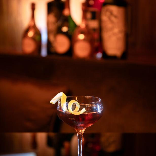Ein Cocktail mit einer Zitronenspirale steht auf einem Tisch vor einer Bar.