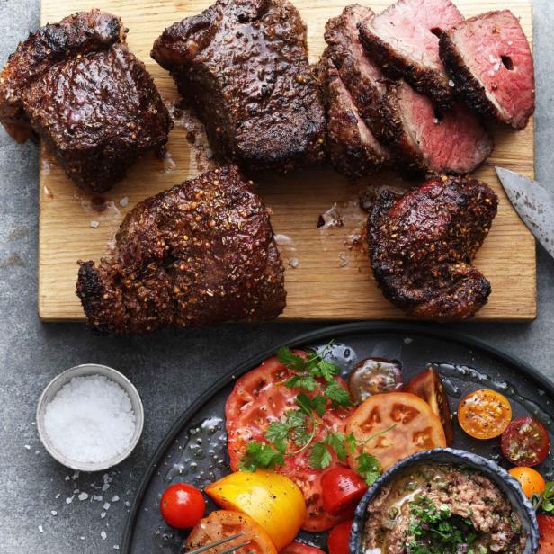 Picanha-Steaks auf einem Holzbrett, serviert mit einem Tomatensalat und Bohnencreme.