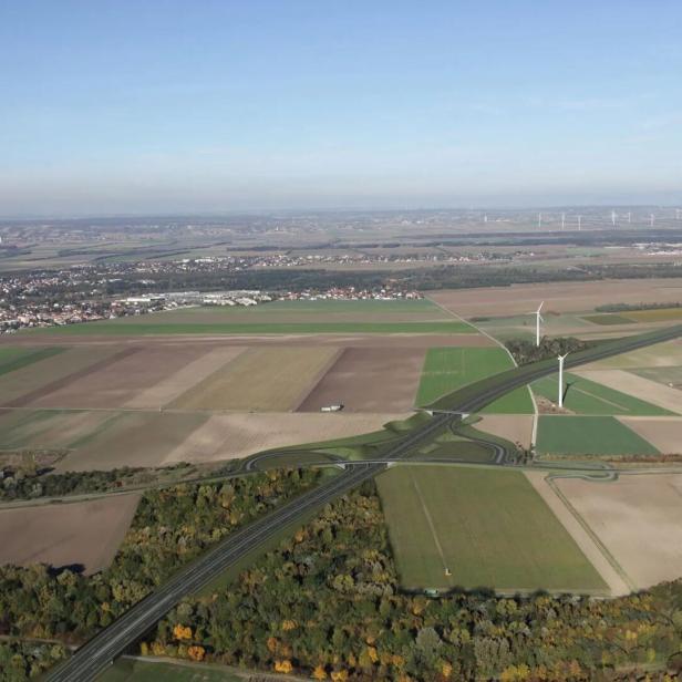 Luftaufnahme einer Autobahn, die durch Felder und an Windrädern vorbei führt.