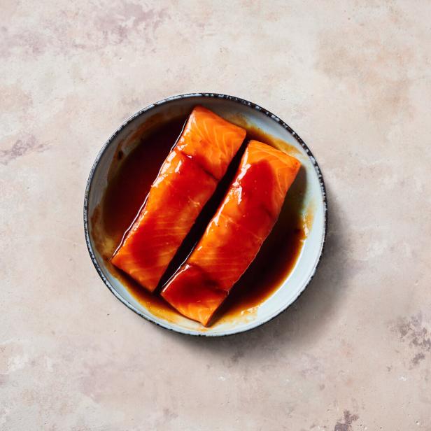 Zwei Lachsfilets in Teriyaki-Marinade in einer Schüssel.