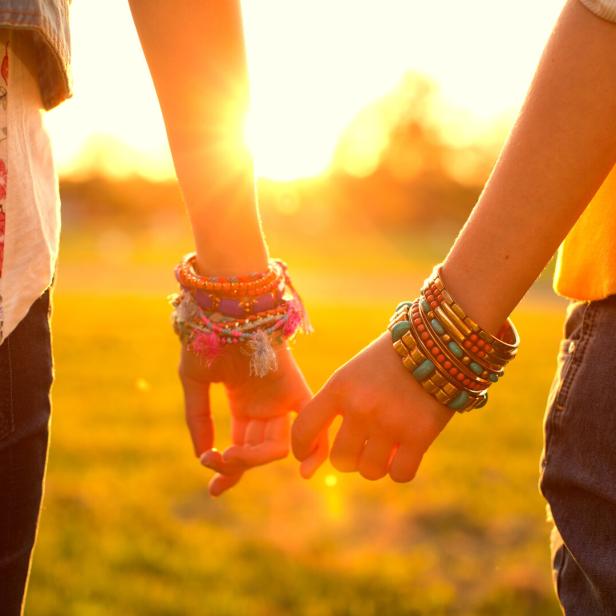 Zwei Personen halten Händchen, beide tragen bunte Armbänder.