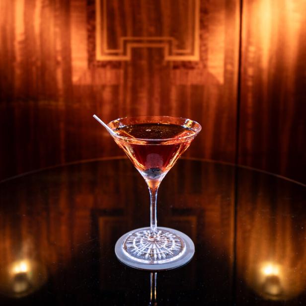Ein Manhattan-Cocktail steht auf einem Tisch vor einer holzvertäfelten Wand.
