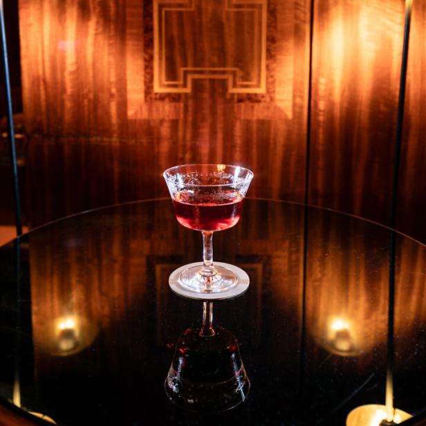 Ein Cocktail in einem eleganten Glas steht auf einem schwarzen Tisch.