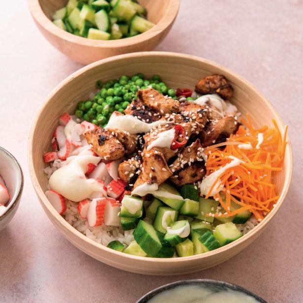 Eine Poke Bowl mit Reis, Hähnchen, Gemüse und Krabbenimitat wird mit Soße garniert.