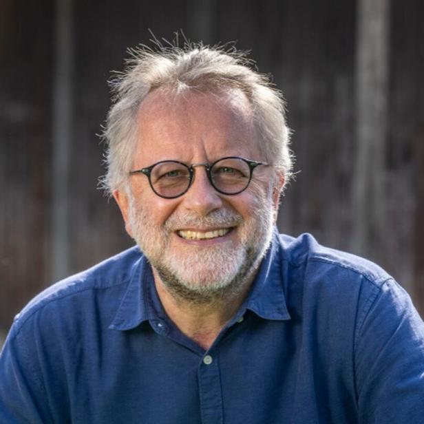 Ein lächelnder Mann mit Brille und Bart trägt ein blaues Hemd.
