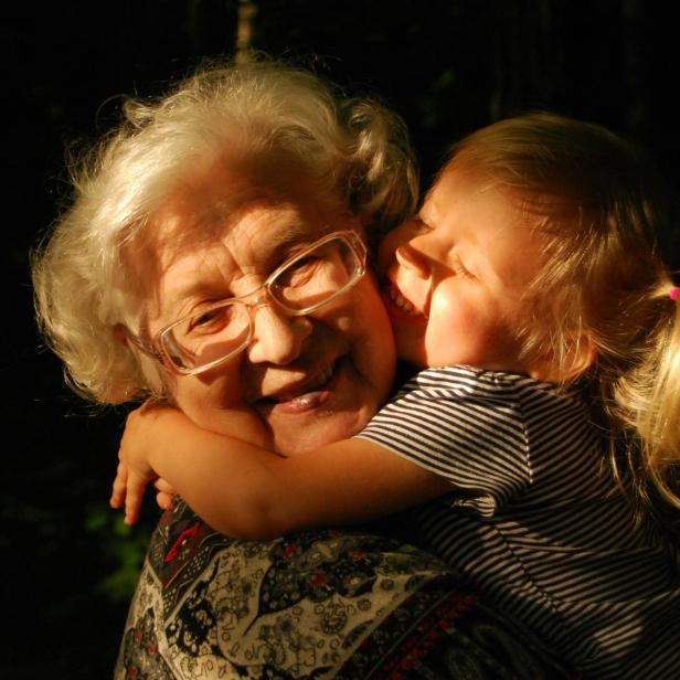 Ein schwarzes Foto, auf dem eine Oma mit ihrer kleinen Enkelin in einer Umarmung zu sehen sind. 