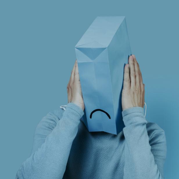 Eine Person mit einer blauen Papiertüte mit traurigem Gesicht über dem Kopf.