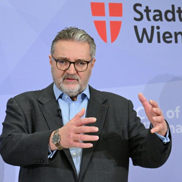 Peter Hacker steht gestikulierend vor einer Wand mit einem Logo der Stadt Wien.