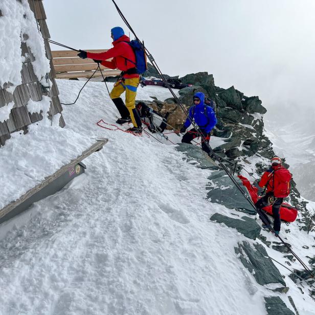 Drei Bergsteiger arbeiten an einem Gebäude in einer verschneiten Berglandschaft.