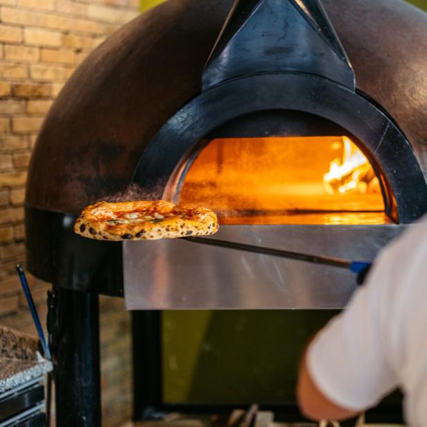 Ein Mann schiebt eine Pizza in einen Ofen.
