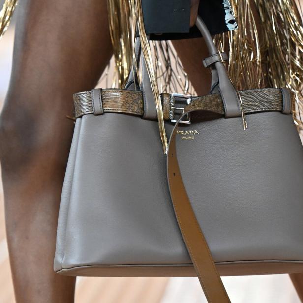 Eine graue Prada-Handtasche mit goldenen Akzenten wird auf einem Laufsteg präsentiert.