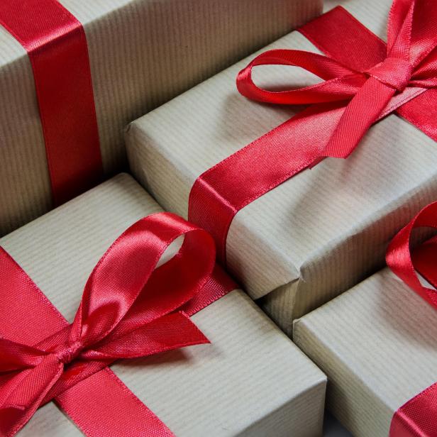 Vier Geschenke mit roten Schleifen in papierfarbenem Geschenkpapier.