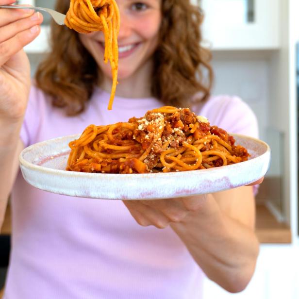 Eine Frau hält einen Teller Spaghetti Bolognese in der Hand.